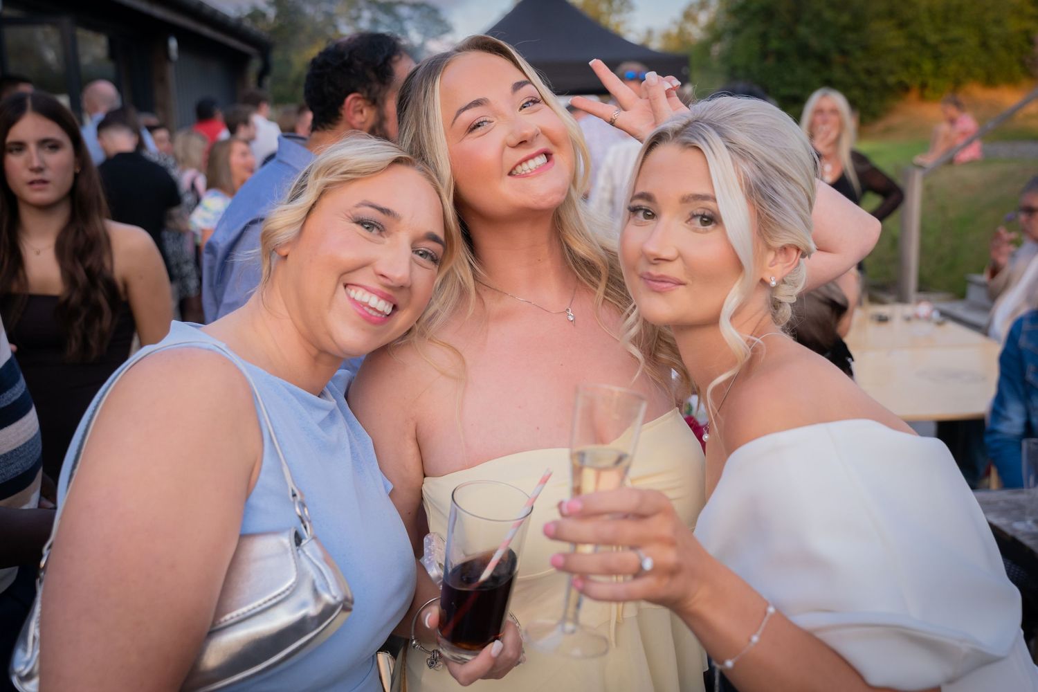 A group of friends laugh and embrace while celebrating at an outdoor party during sunset.