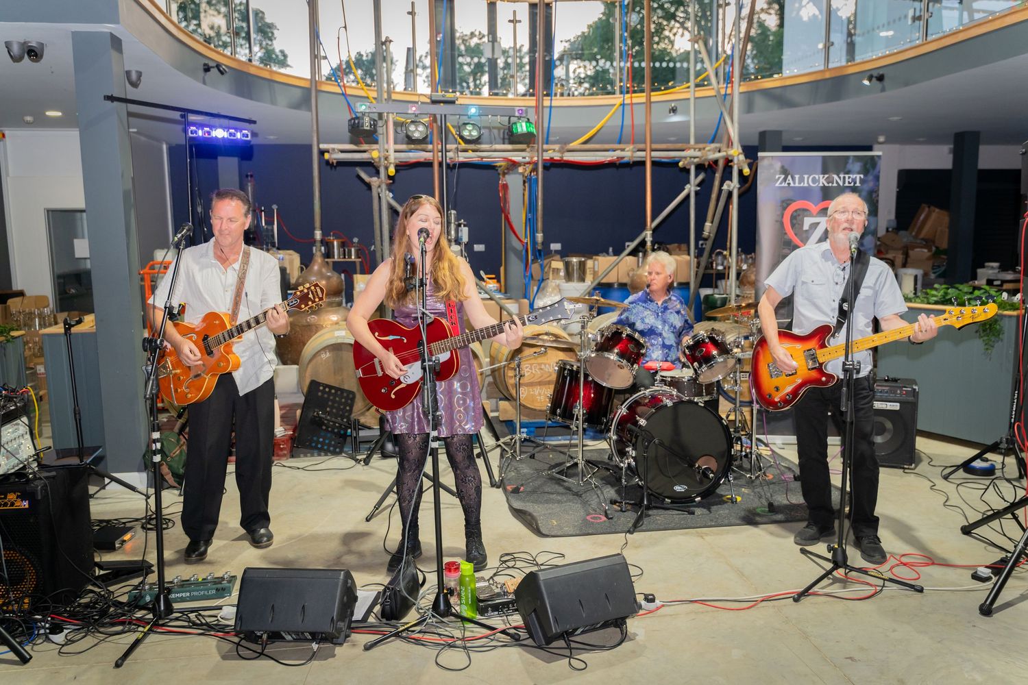 Musicians perform together in a studio space with instruments and equipment visible across multiple connected rooms.