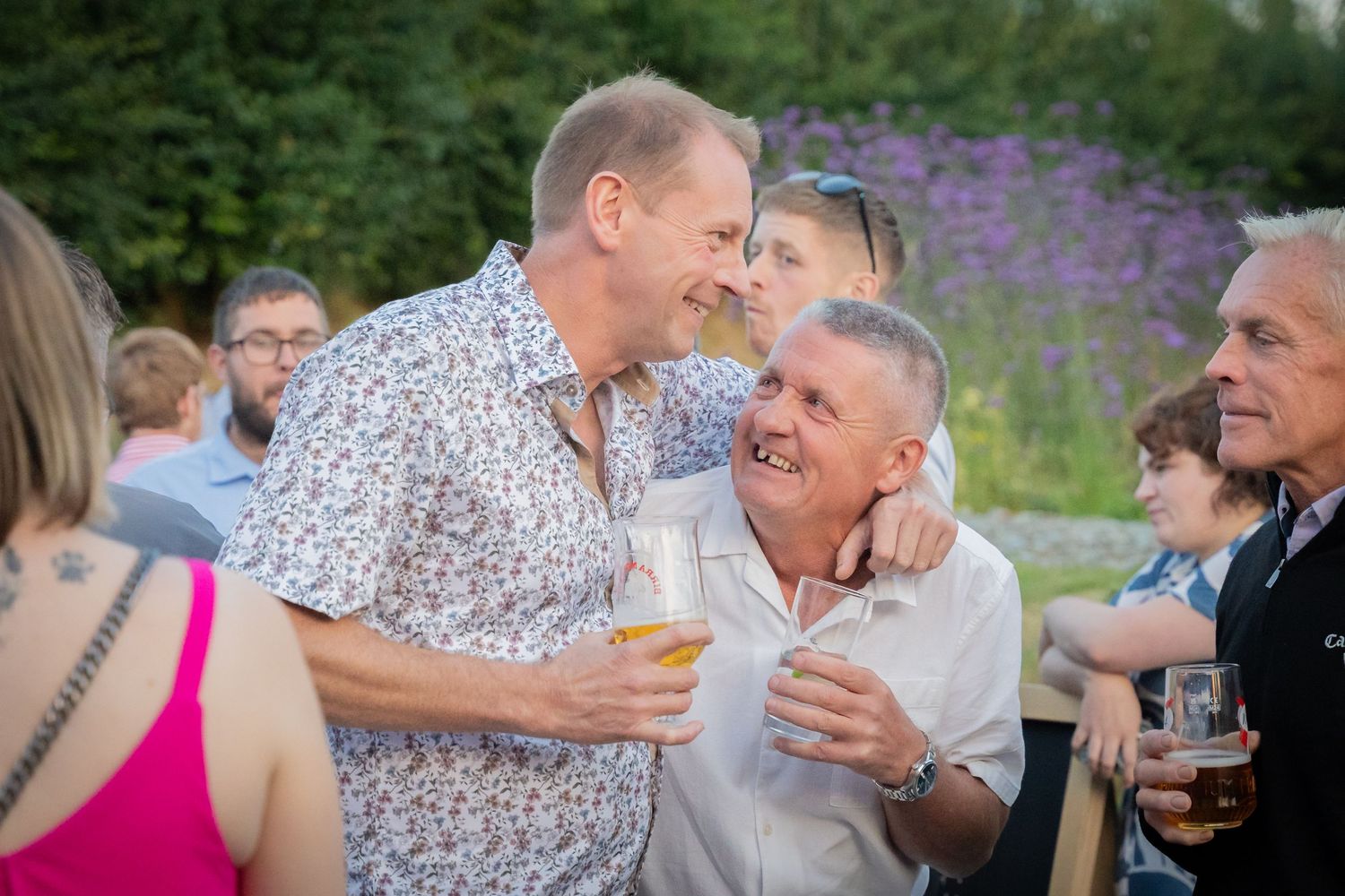 Wedding guests enjoy drinks and conversation during an outdoor summer reception in a garden setting.