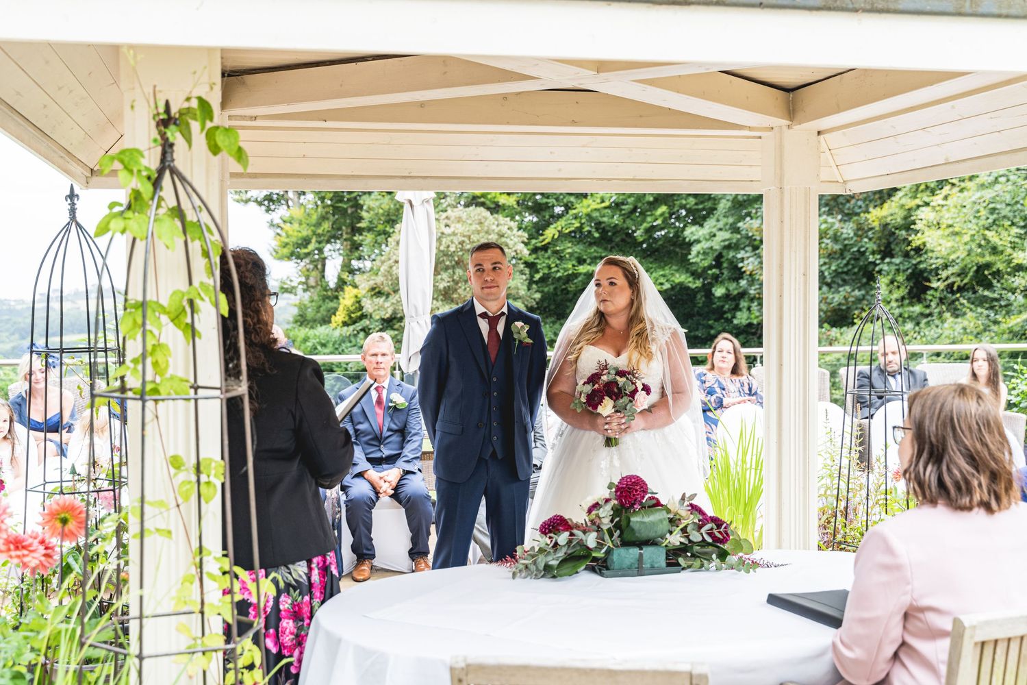 Outdoor wedding ceremony under a white gazebo decorated with floral arrangements.