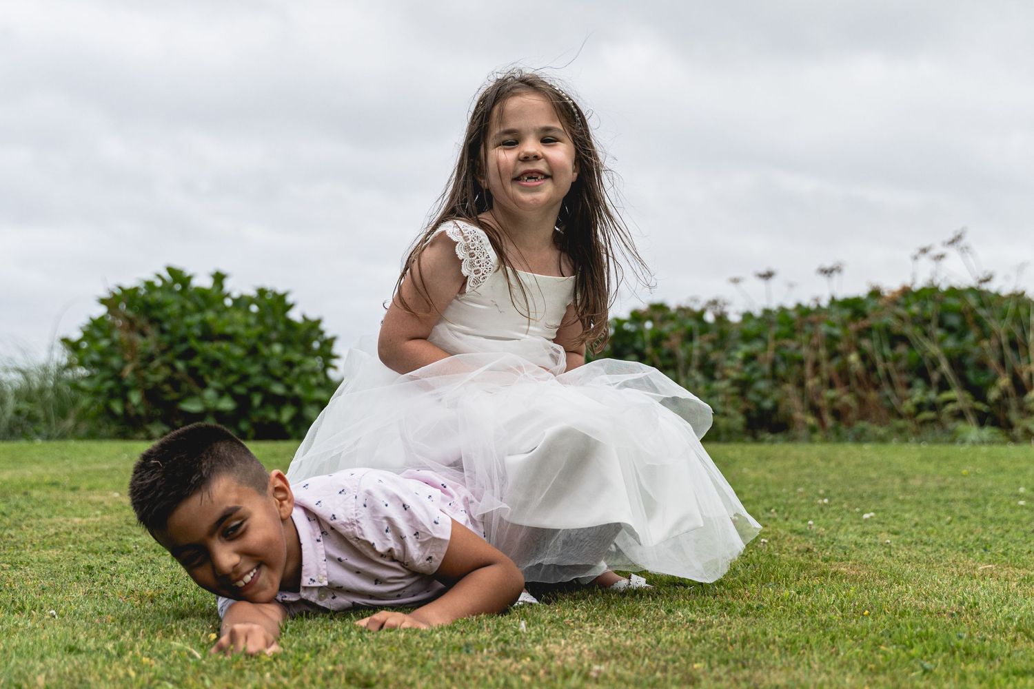 Children in formal attire playing and laughing on grass during wedding. Cornwall Wedding Photographer. Cornwall Wedding.
