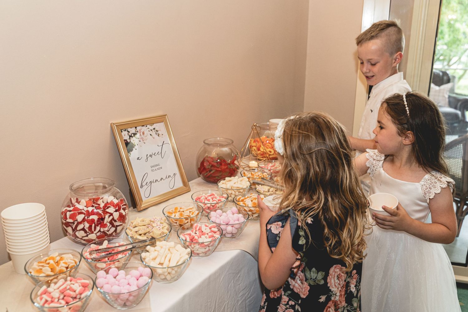 Wedding guests selecting treats from candy buffet table with pink and orange sweets. Cornwall Wedding Photographer. Wedding Treats.
