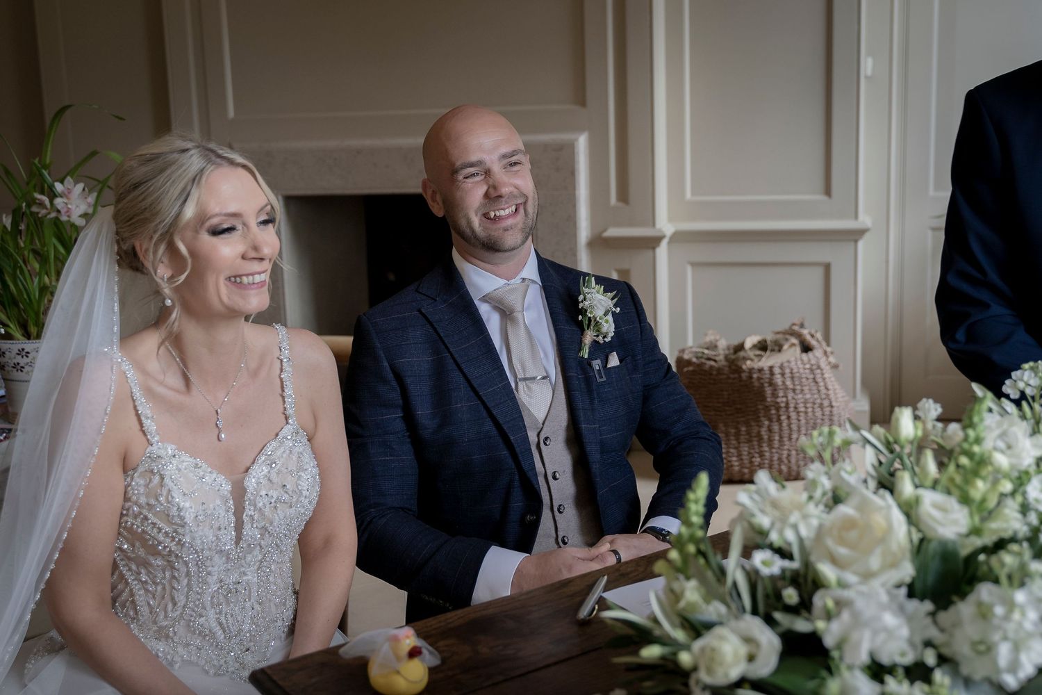 Wedding couple shares a candid moment during reception with elegant floral decorations. Shilstone House Wedding. Devon Wedding Photography.