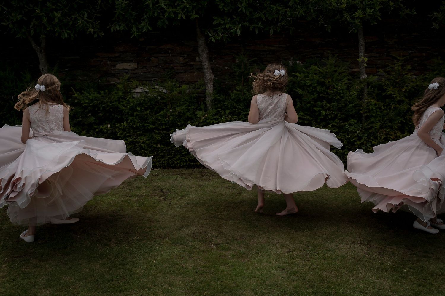 Three dancers in white dresses twirling in a garden setting at dusk.
