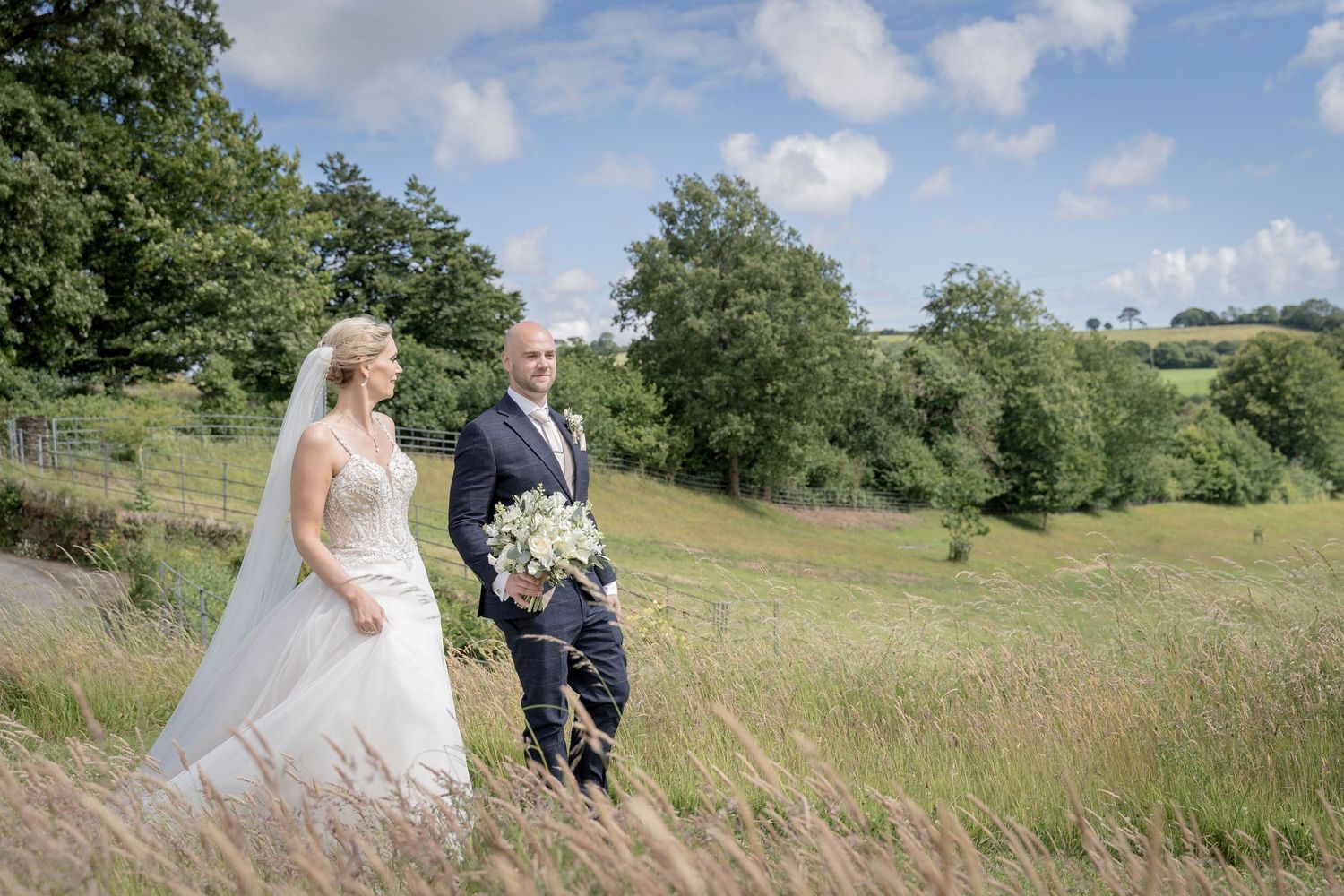 Couple in wedding attire posing in scenic rural landscape with hills and greenery.  Shilstone House, Devon Wedding. Devon Photographer.