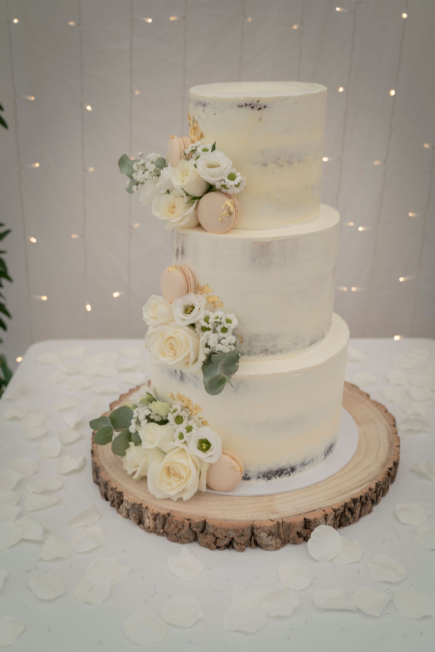 Elegant four-tier white wedding cake decorated with roses and eucalyptus on rustic wood slice base.