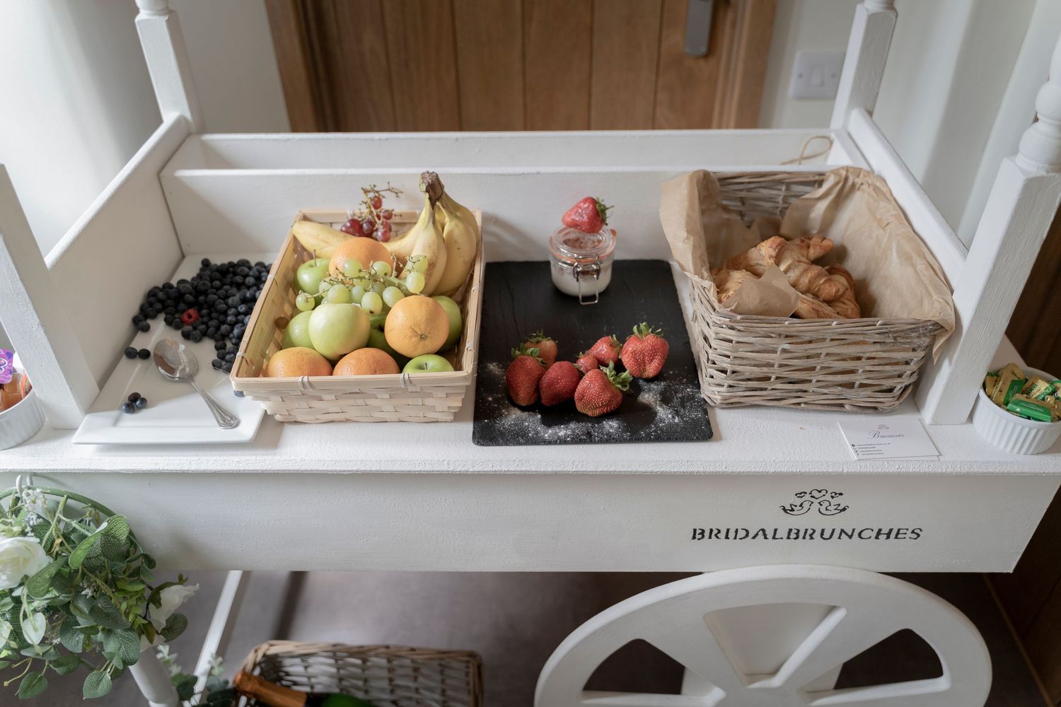 Rustic baskets filled with fresh fruits and snacks arranged on white shelf.