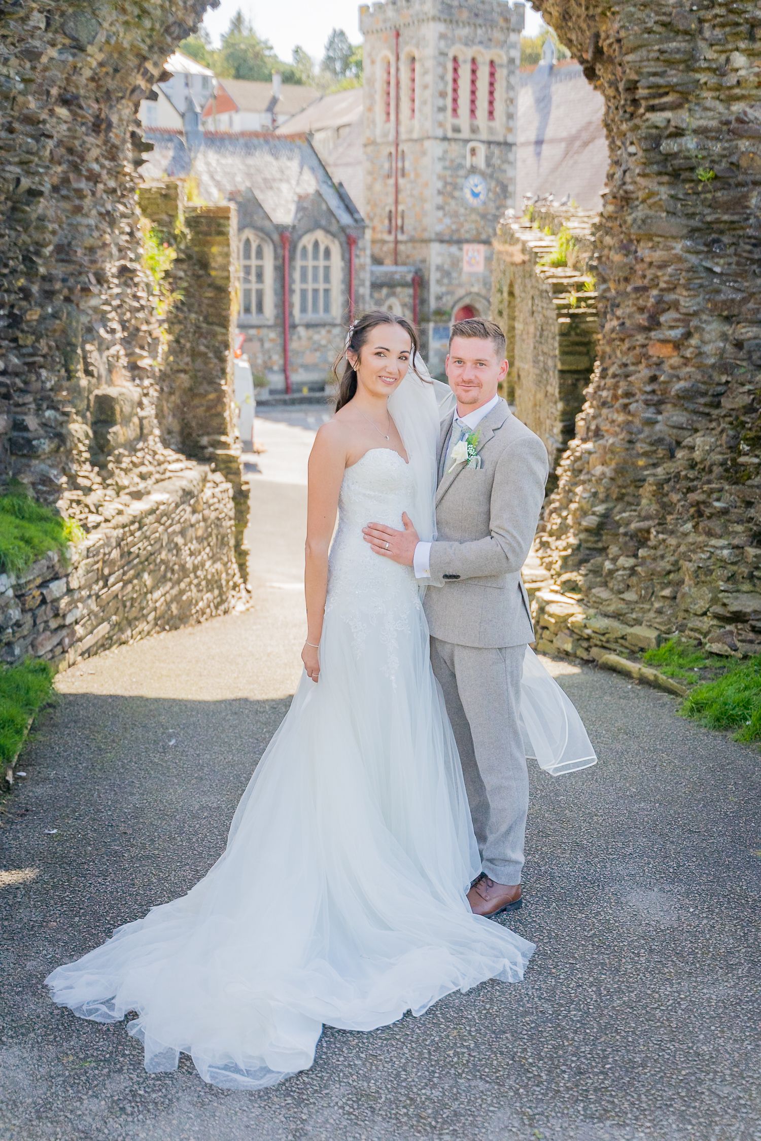 A wedding couple poses in front of stone archways and a historic church building on their special day.