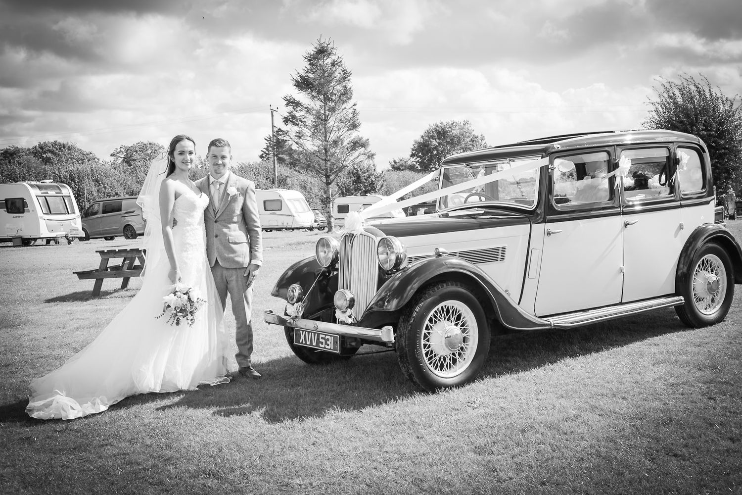 Classic vintage white car parked on grass with wedding party in black and white photography.