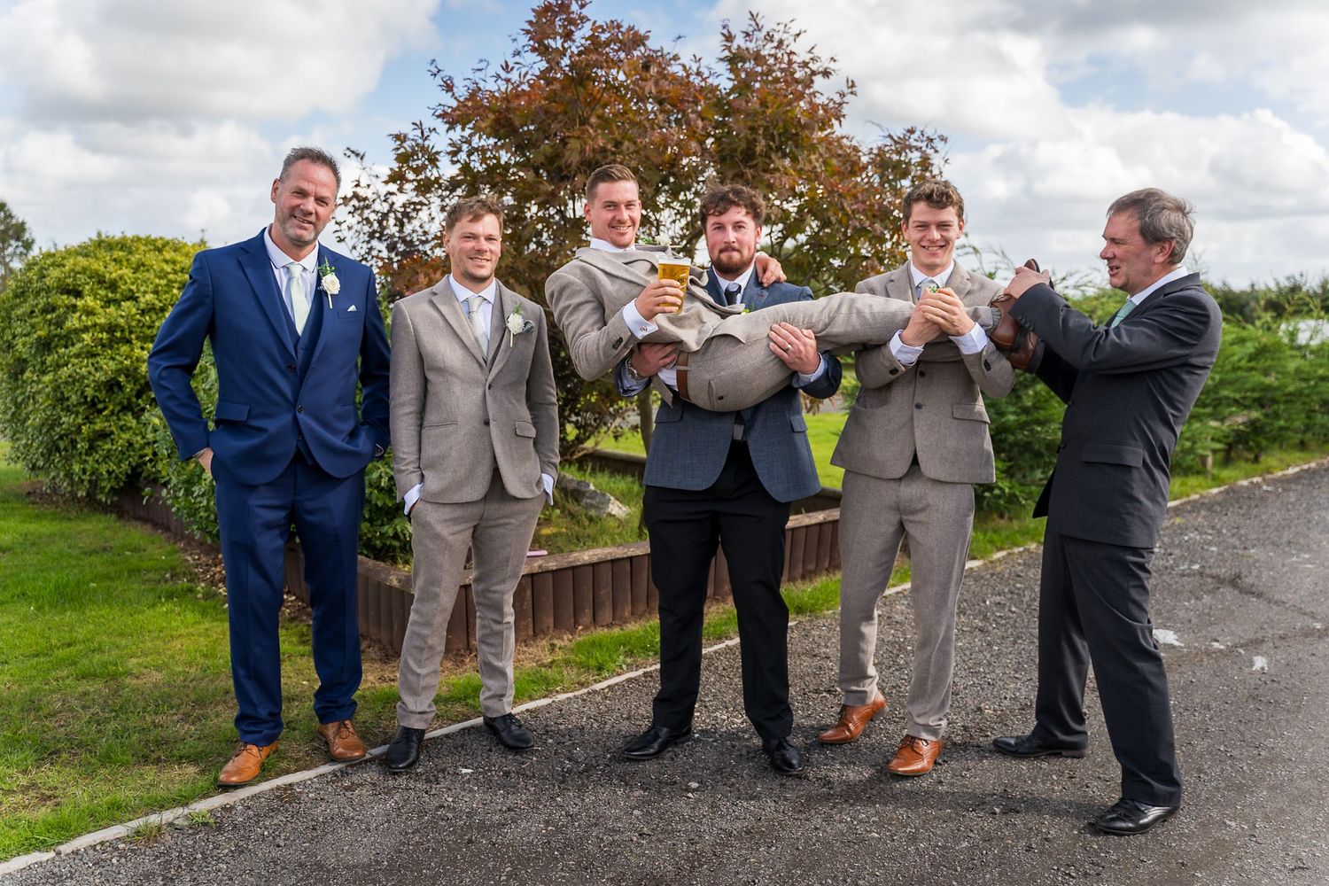 Groomsmen in suits share a celebratory moment outdoors on a cloudy day.