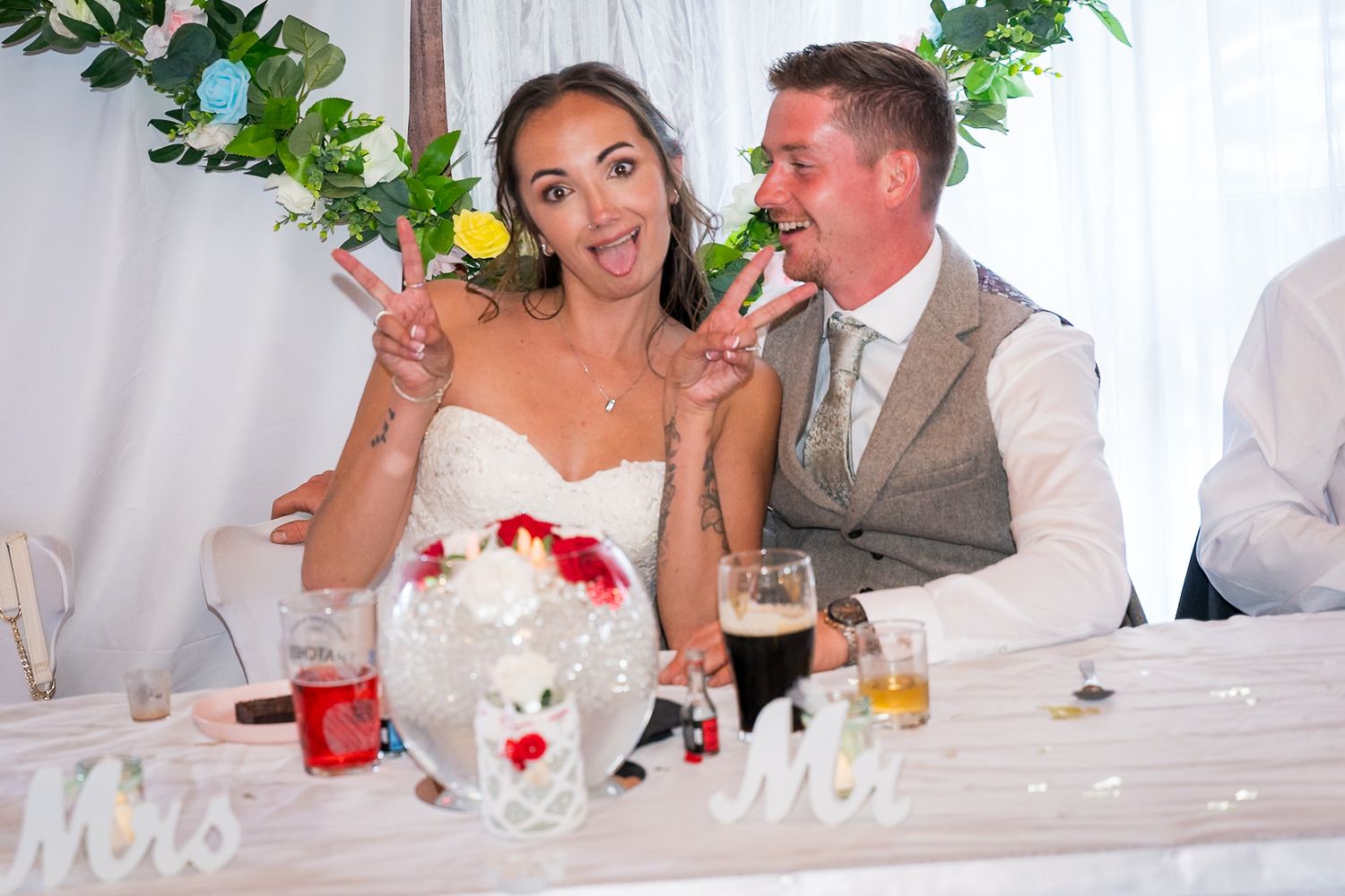 A wedding reception table decorated with white linens and red floral accents during a celebratory moment.
