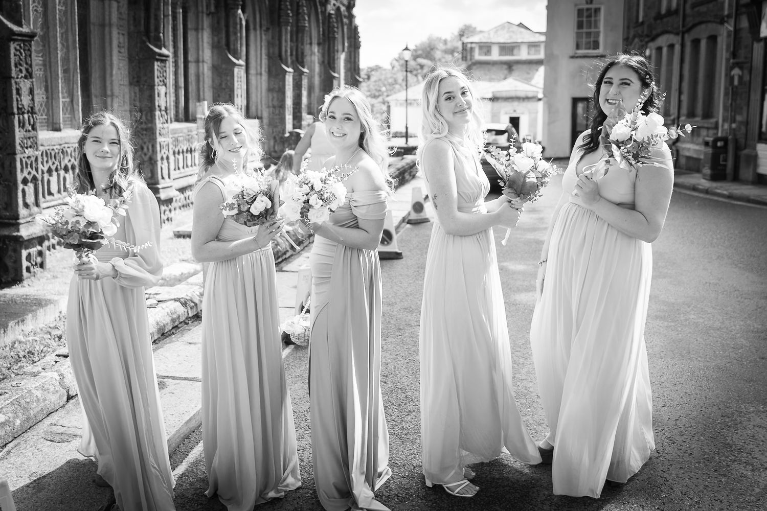 Wedding party in white dresses poses together outside a traditional church building.