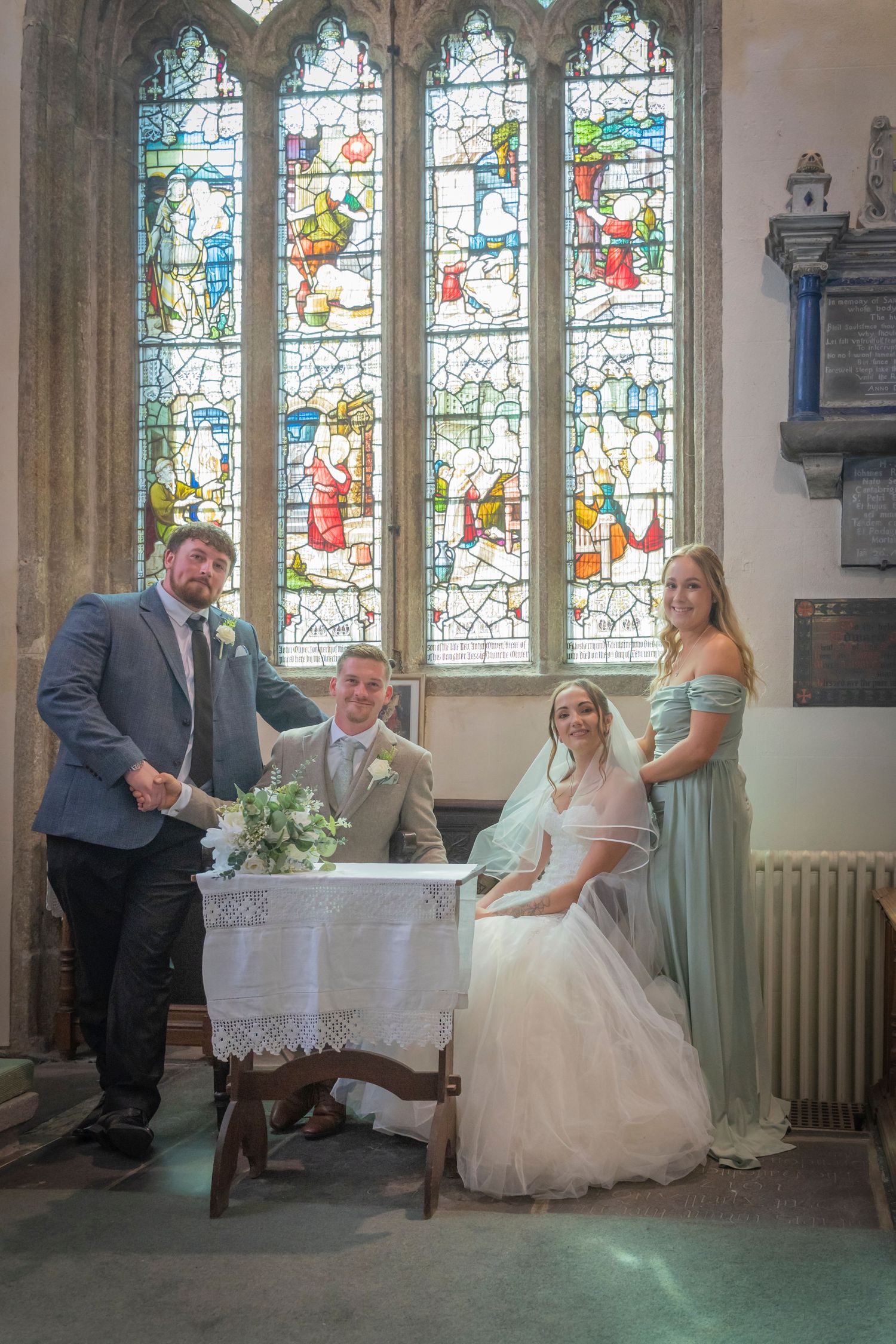 Wedding party gathered in church interior with beautiful stained glass windows.