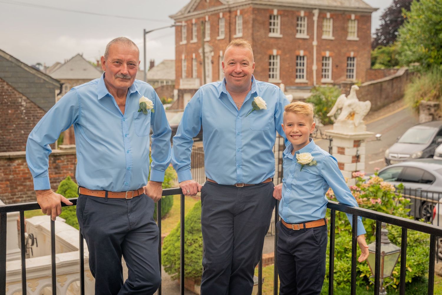 Two people in matching blue shirts stand together on stone steps outside a historic brick building.