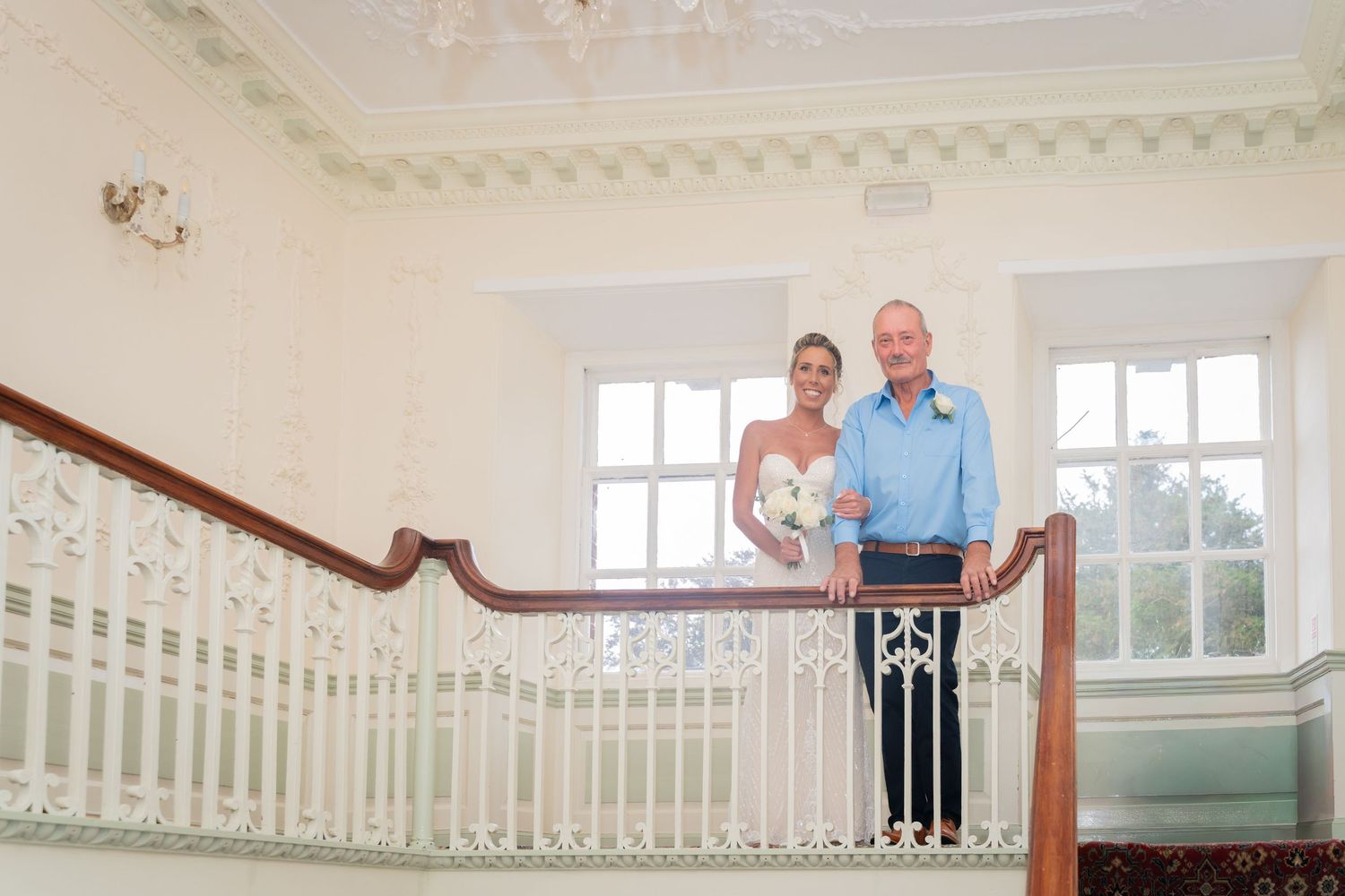 Elegant white staircase with wooden handrail and decorative wallpaper in a traditional home interior.