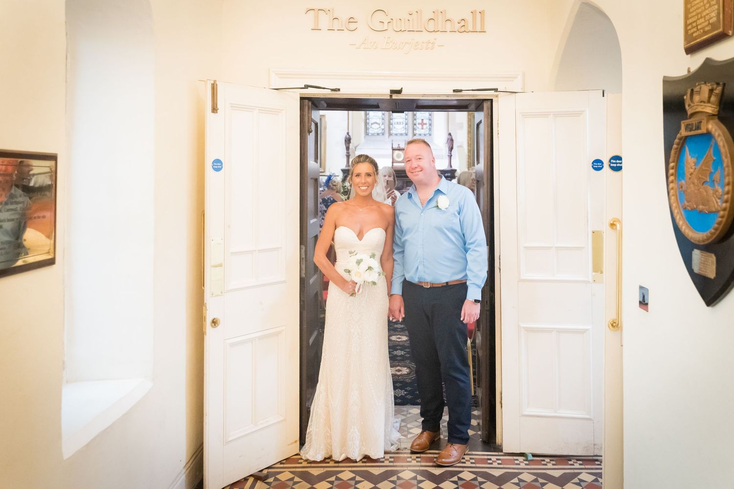 A couple stands together in a doorway at The Guildhall venue, with decorative walls and artwork visible in the background.