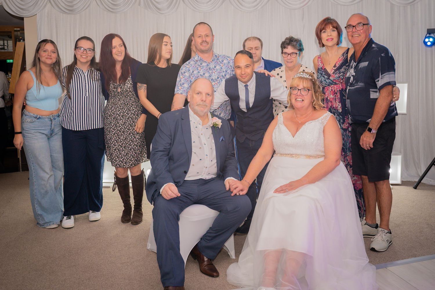 Wedding reception guests gather for group photos in an elegant white-draped venue setting.