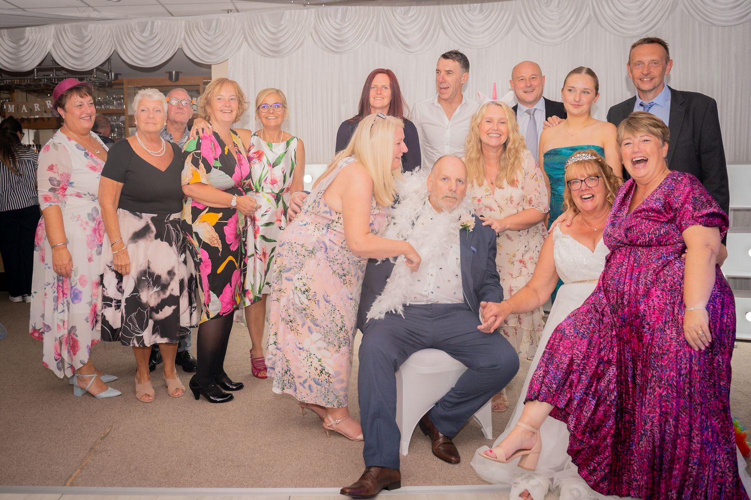 A group in formal attire poses together at a celebration event with decorative white drapes in the background.