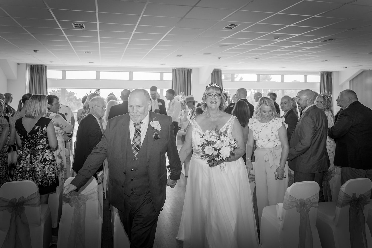 A black and white panoramic collage of wedding reception scenes showing guests mingling and dancing in a banquet hall.