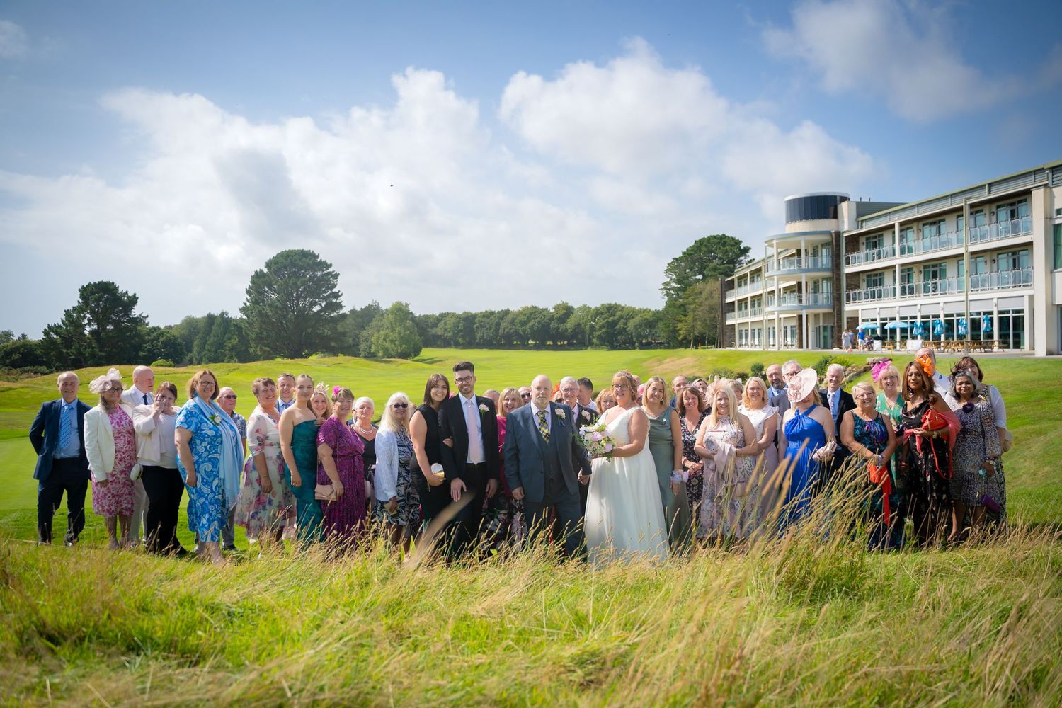 A large group of wedding guests lined up in colorful attire against a scenic outdoor landscape.