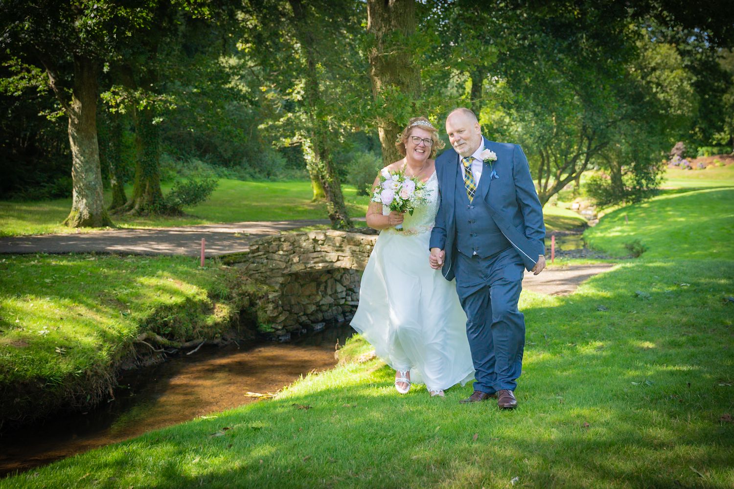 A couple shares a romantic moment in a lush garden setting with sunlight filtering through the trees.