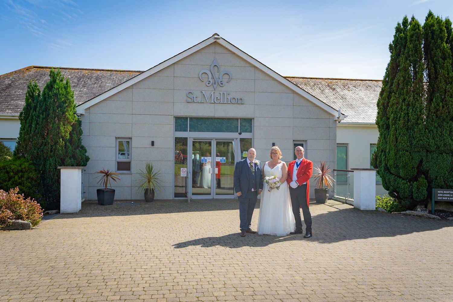 Exterior view of a white wedding venue building with elegant columns and cypress trees in the landscaping.