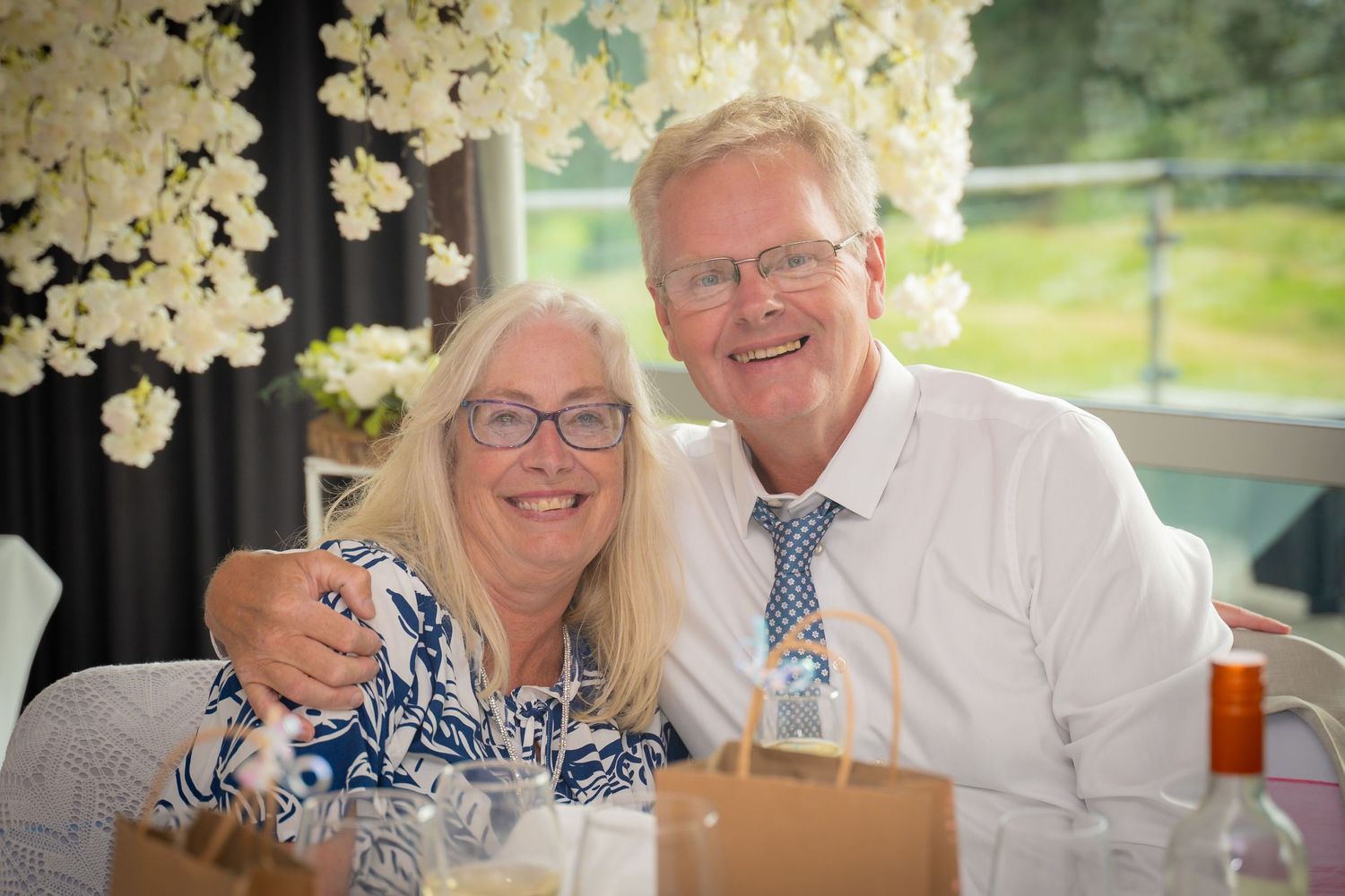 People celebrating at a wedding reception with white floral decorations and table settings in a bright venue.