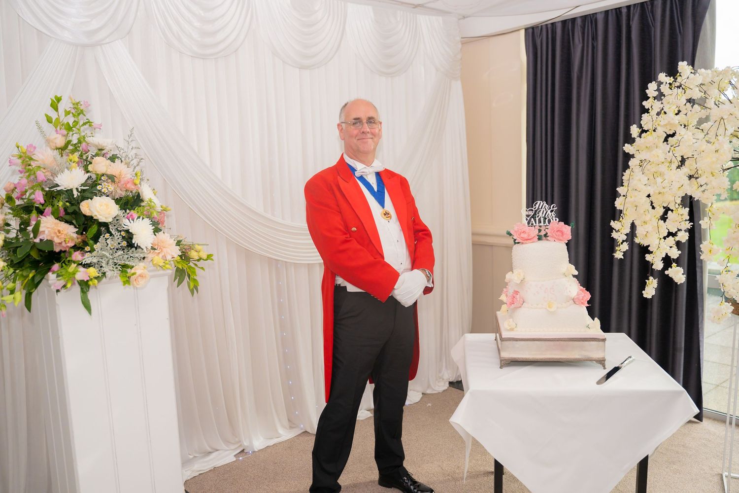 Wedding reception setup with white drapes, floral arrangements, and decorative elements.