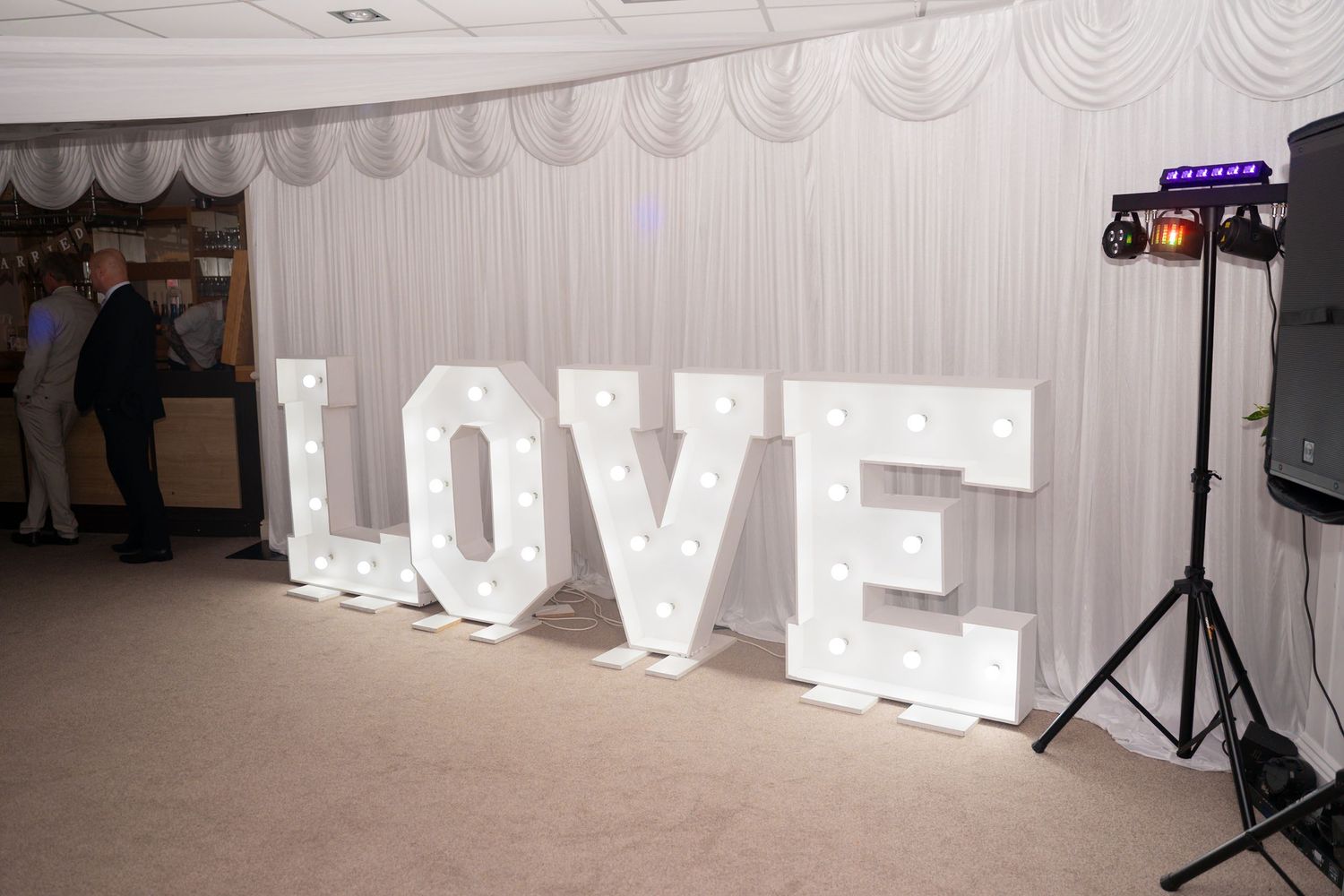 Illuminated white LOVE letters create a romantic backdrop display at an indoor event venue.