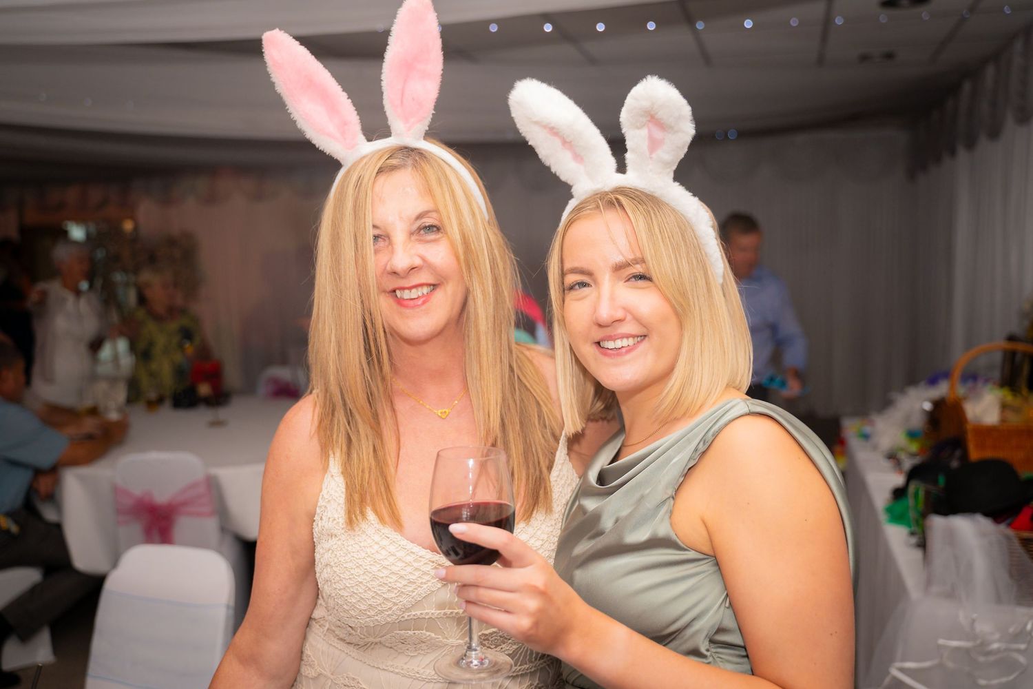 Party guests wearing pink bunny ears pose together at a festive indoor celebration with decorations.