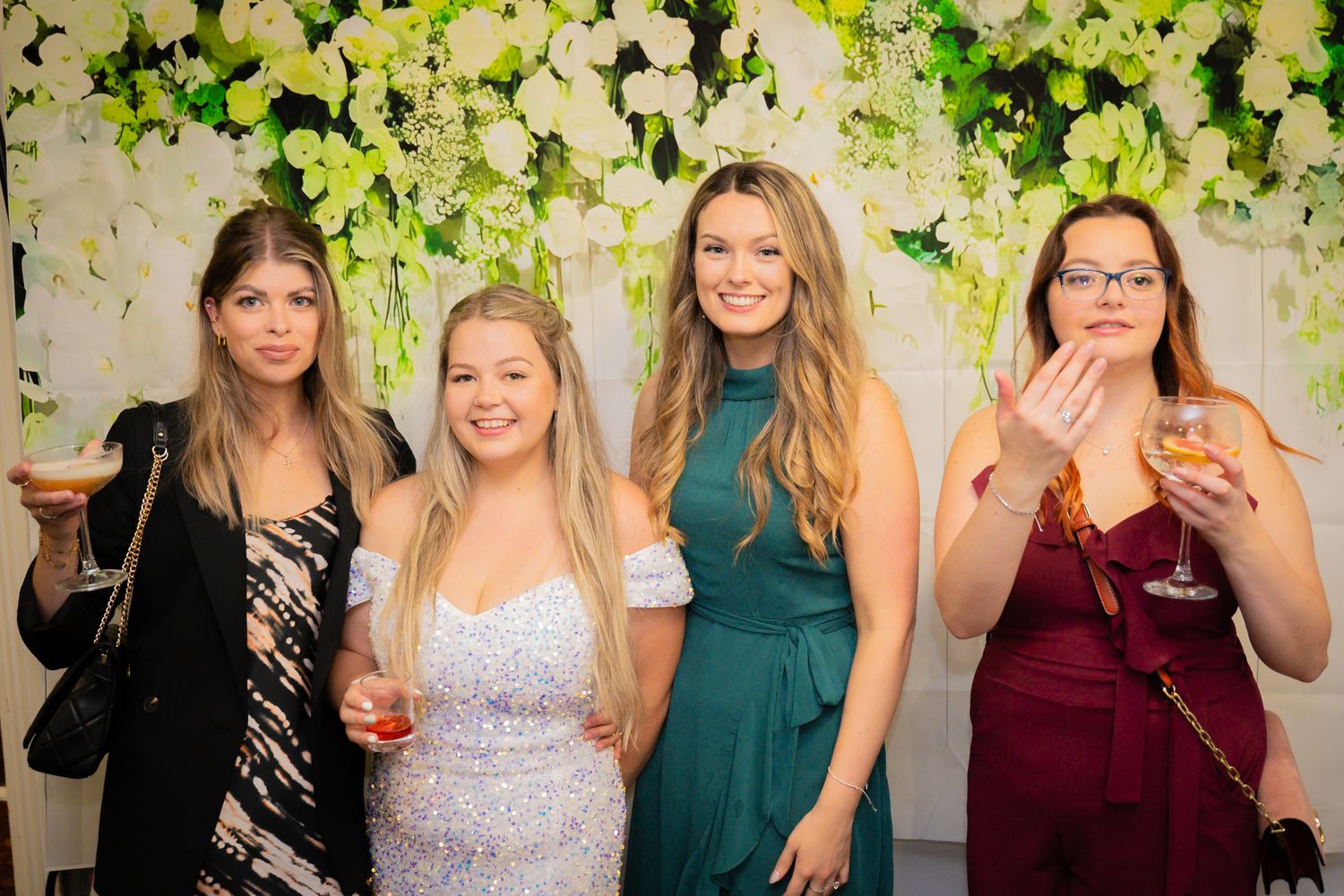 A group of friends in formal attire gather together at a social event, smiling and posing for photos.