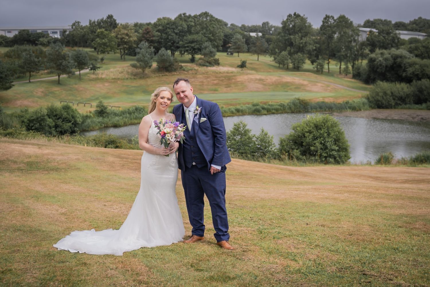 A couple shares romantic moments during their outdoor wedding photoshoot near a scenic lake and rolling hills.
