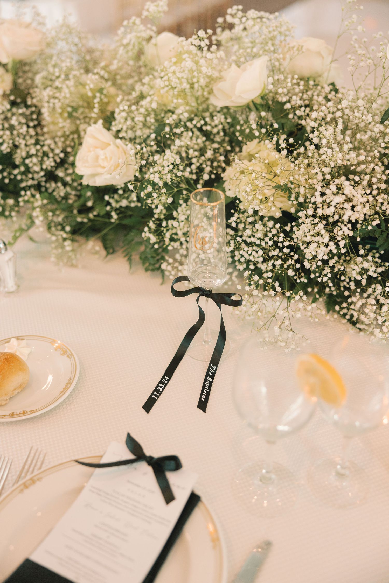 Wedding reception table with white roses, babys breath centerpiece, black ribbon name cards and glassware.