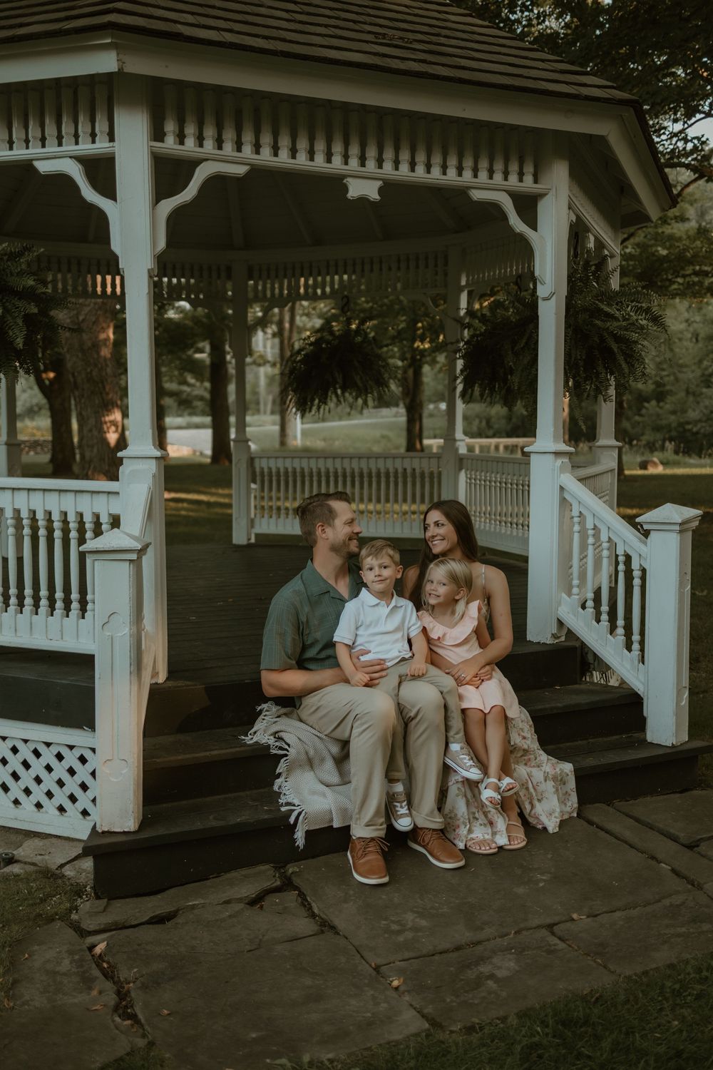 A family shares tender moments together while sitting in a white wooden gazebo during golden hour.