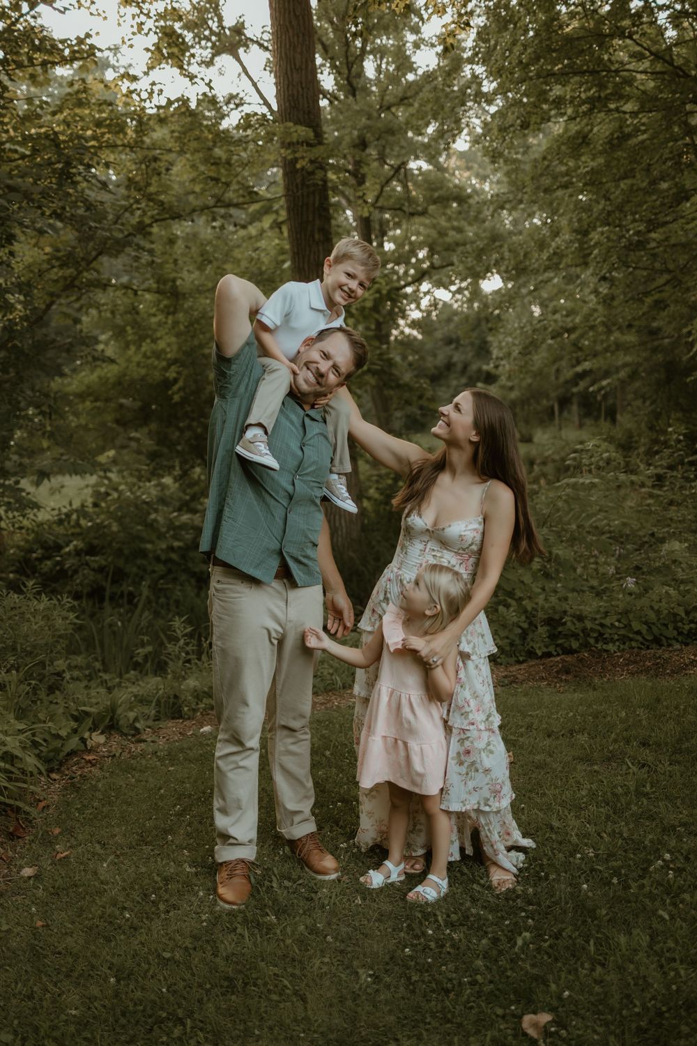 A joyful family plays and laughs together on grassy ground during an outdoor photo session.