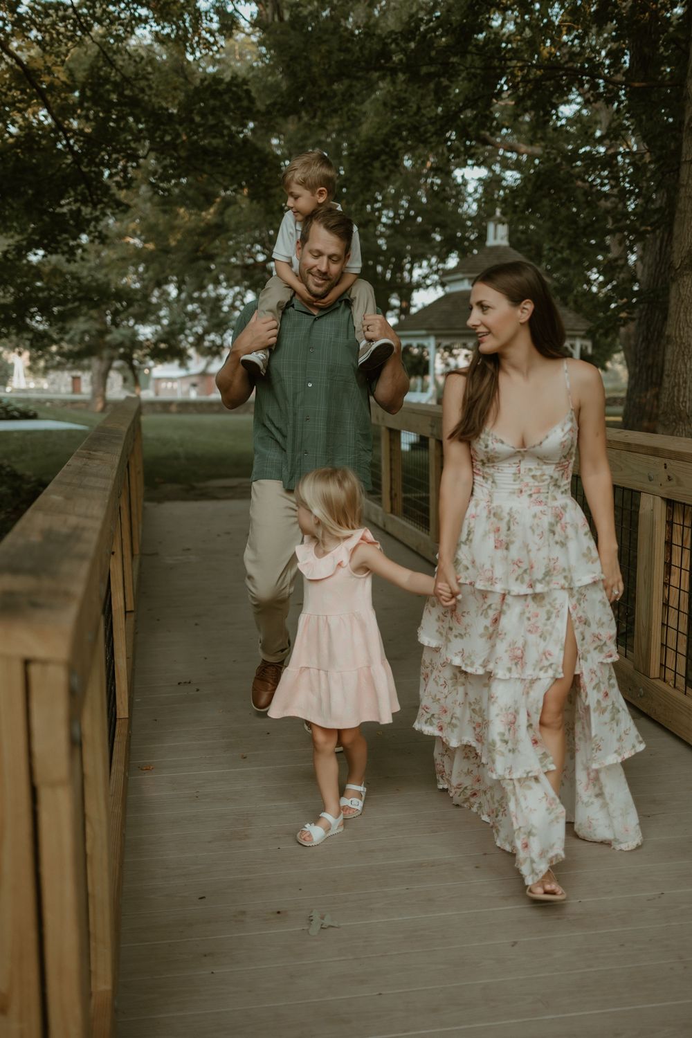 A family walks together along a wooden boardwalk through a park on a summer evening.