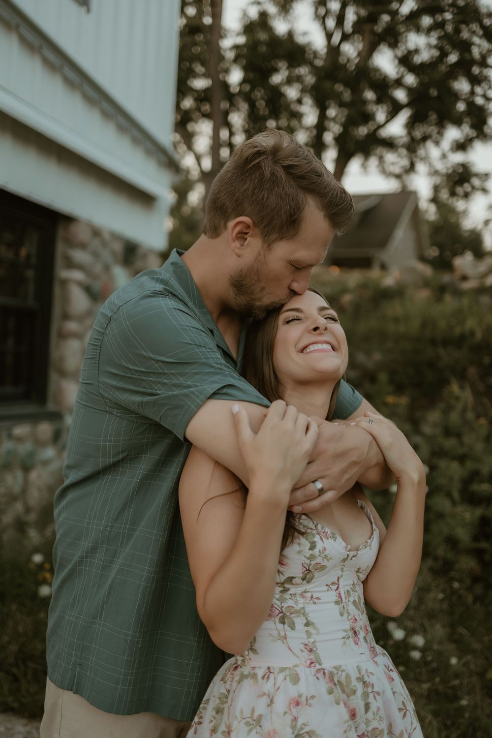 A couple shares a tender moment outdoors, with the person in a floral dress and green shirt embracing lovingly.