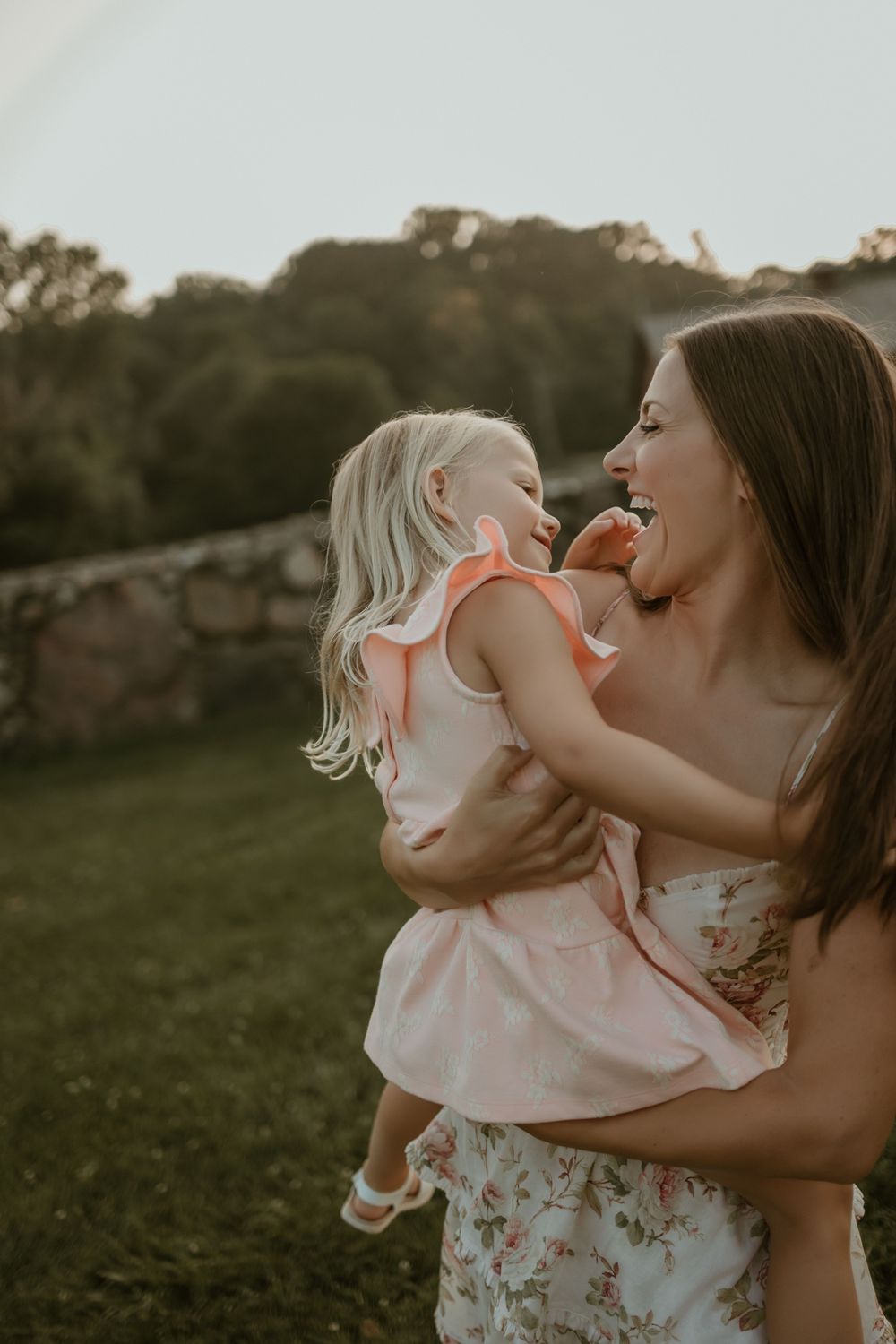 Mother and daughter share a tender moment in a field at sunset wearing matching floral and pink outfits.