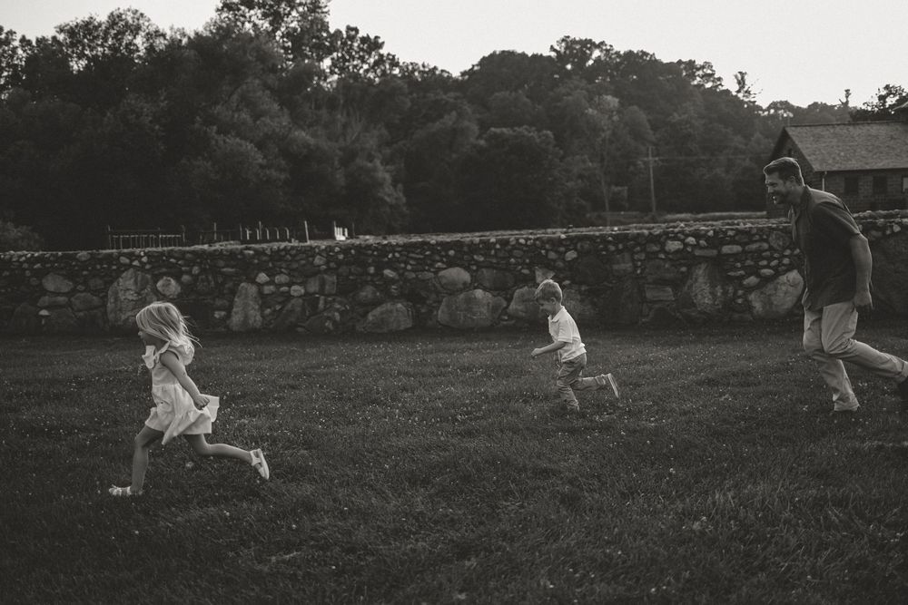 A black and white photo where a dad chases his two young kids