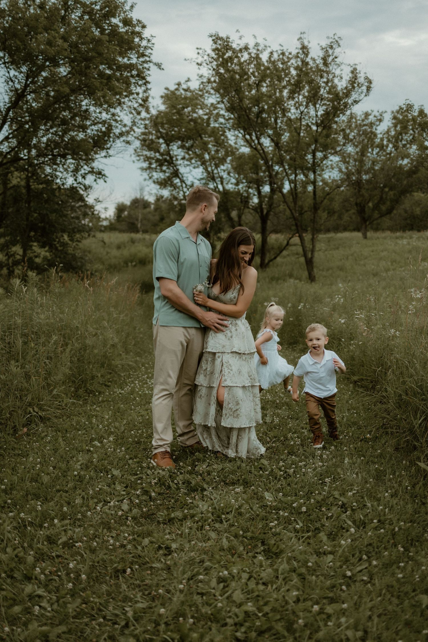 A family stands together in a green meadow with trees in the background on an overcast summer day.