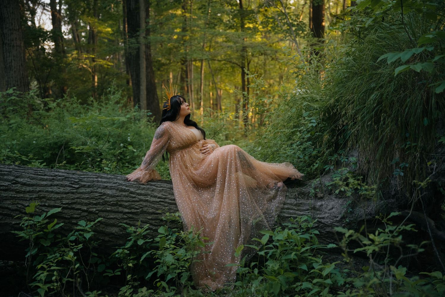A flowing peach dress catches golden light in a mystical forest setting while draped across a fallen log.