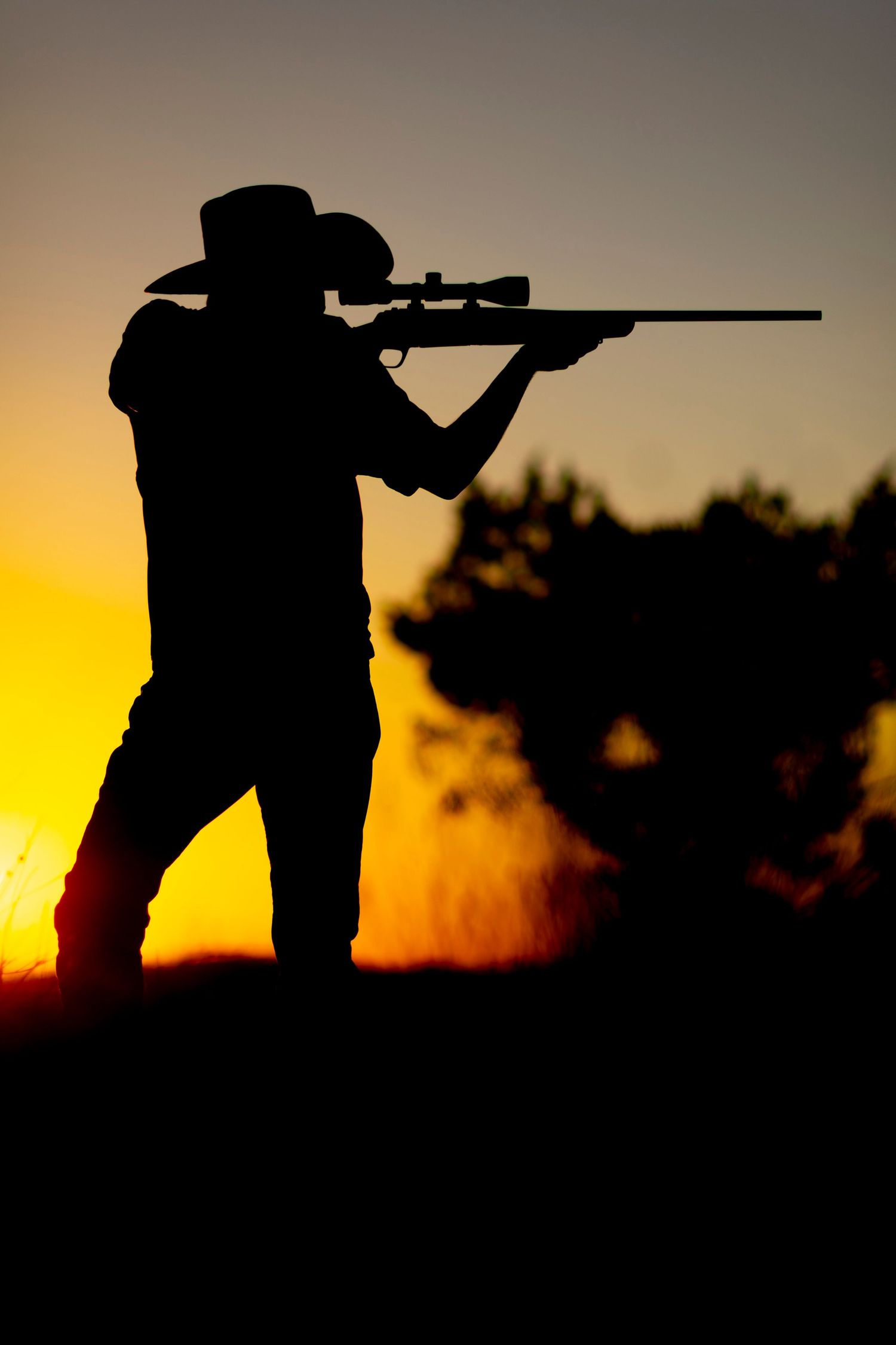 Silhouette of a cowboy aiming a rifle against a vibrant orange and yellow sunset sky.