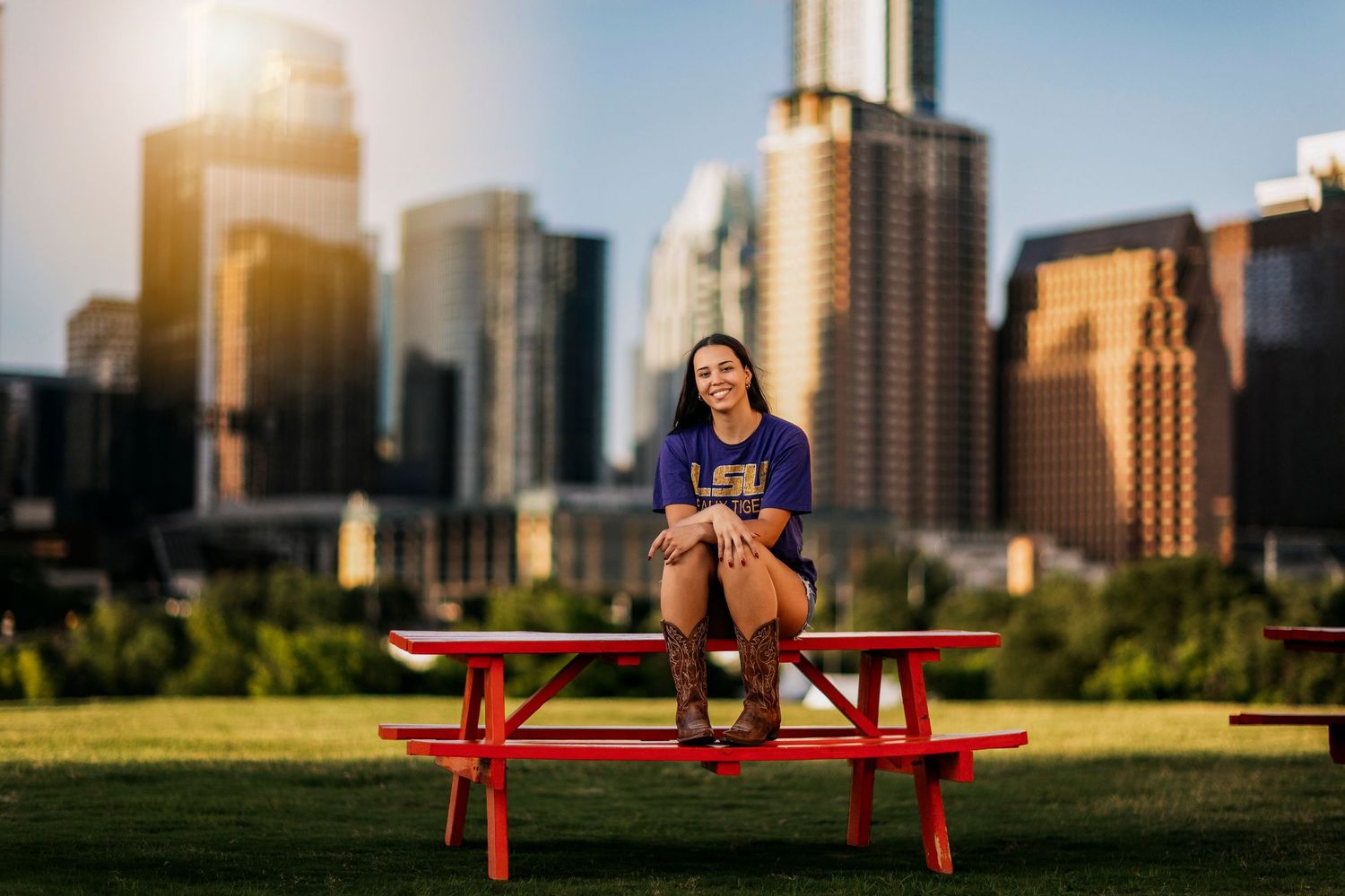 Young woman sitting on a red picnic table smiling with Austin Texas city skyline in the background.