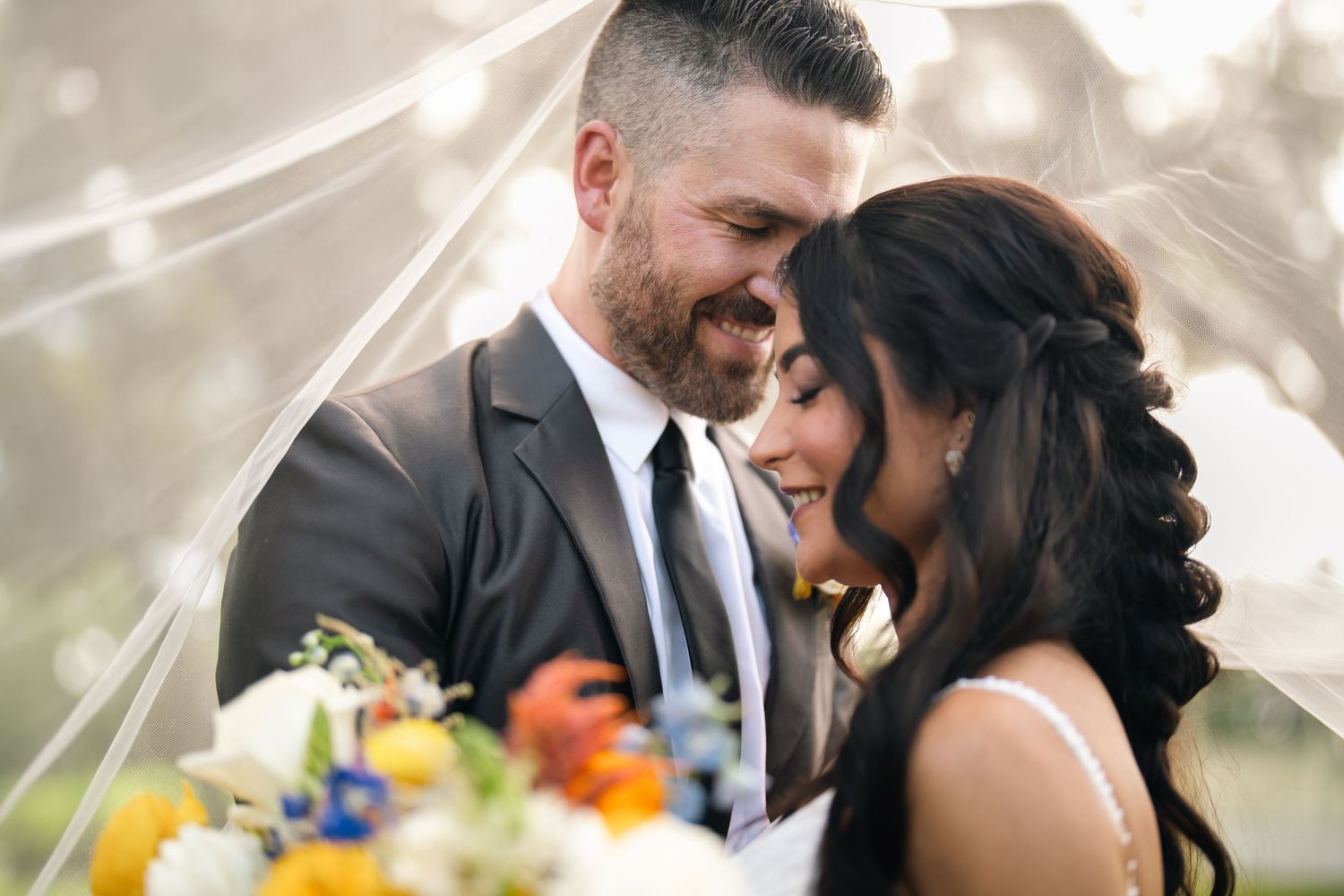 Joyful bride and groom share a laugh together outdoors under moss-covered trees on their wedding day.
