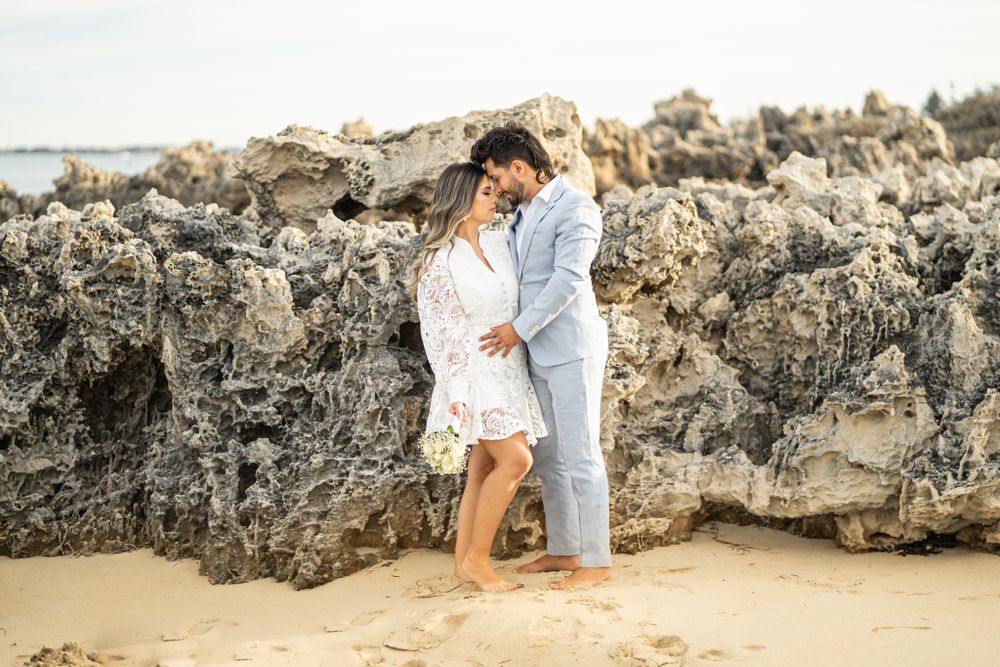A couple shares an intimate moment against weathered coastal rocks at the beach.