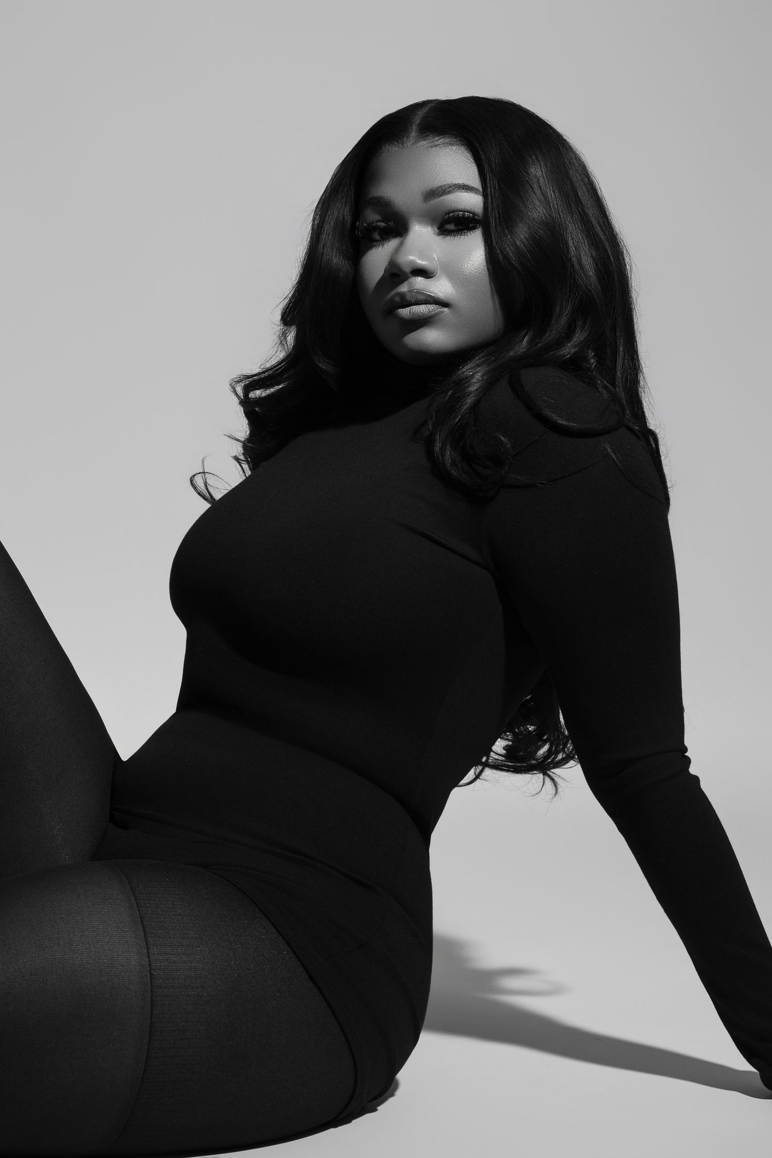 A person in a brown long-sleeved dress sits in a relaxed pose against a light gray background.