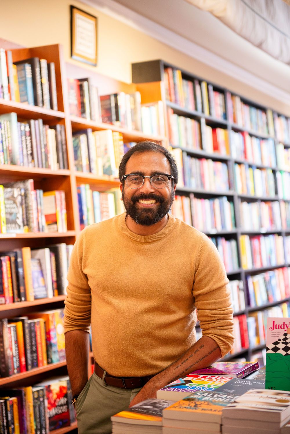 Man in tan turtleneck browses books in library with full bookshelves behind him.