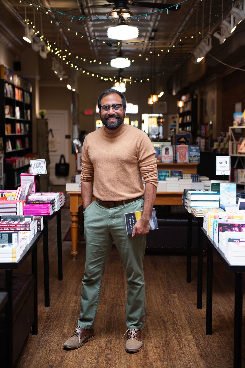 Person browsing in a cozy bookstore with string lights and wooden floors.