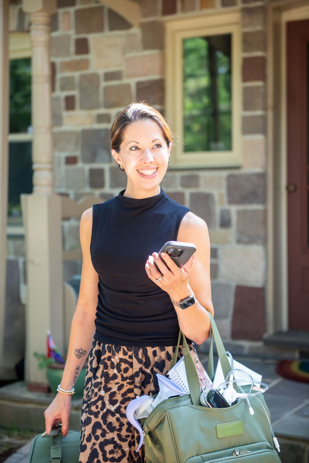 Person in black sleeveless top with leopard print skirt holding phone and bag outside stone building.