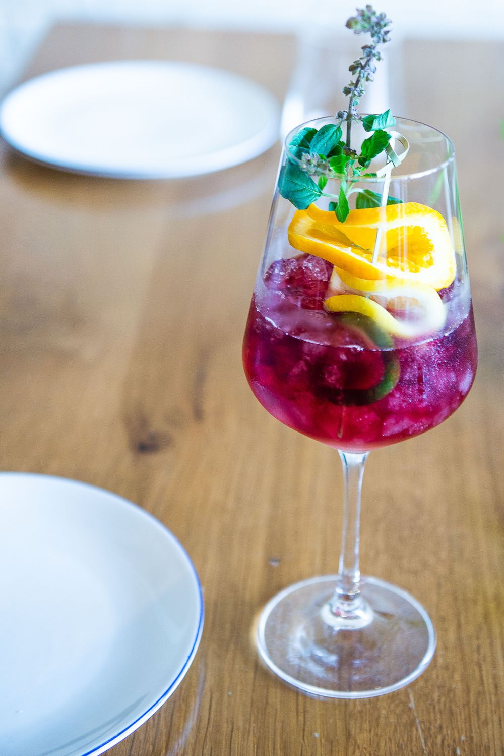 Colorful cocktail with orange slice, herbs and ice in wine glass on wooden table.